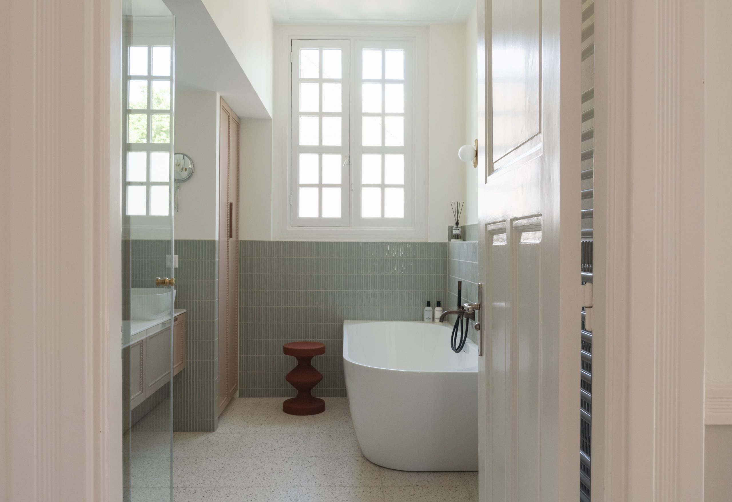 Badkamer totaaloverzicht met klassieke raampartij, vrijstaand bad, groene verticale tegels, terrazzo vloer en maatwerk kastenwand, interieurontwerp atelier Det Wageningen